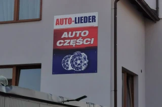 Plakat promujący sklep motoryzacyjny Auto‑Lieder na elewacji budynku w Luzino